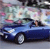 A blue convertible car with a person driving, set against a blurred background of pastel colors and indistinct shapes.
