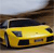 Yellow sports car with dark windows and black accents, positioned on a road under a light sky, viewed from a low angle.