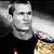 Pixelated grayscale portrait of a person with short hair wearing dark clothing, holding an object with colorful pixelated patterns against a black background.
