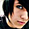 A close-up of a person with short dark hair, blue eyes, and a lip piercing, wearing a dark top against a light background.