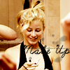A woman with blonde hair in a high bun wears a black halter top and holds a small object while smiling, with partial text overlay reading "Wake Up" on her chest.