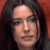 Pixelated close-up of a person with long dark hair against a reddish-brown background, showing facial features and partial shoulder area.