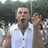 Pixelated image of a man in a white sleeveless shirt with mouth open, surrounded by people, on a bright cyan background with pixelated text.