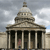 Static pixelated image of a classical building with columns and a domed roof under a cloudy sky.