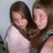 Two people with long brown hair embrace; one wears a light pink top, the other a dark sleeveless top. Text reads "GO FALL IN A HOLE!" in pixelated black letters.