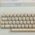 A pixelated keyboard with beige keys and dark brown keycaps, set against a light gray background with a faint blue and cyan horizontal stripe near the top.