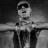 Black-and-white animated icon of a person in cap and sunglasses holding an object with arms extended horizontally.