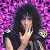 A woman with long dark hair and a black sleeveless top stands against a purple pixelated background, her hand near her face in three