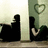 Pixelated image of two silhouetted figures sitting on a floor against a wall with a heart outline, overlaid with blue pixelated text.