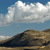 Pixelated landscape showing a mountain under a blue sky with white clouds, rendered in low-resolution style.