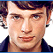 A pixelated image of a person with dark hair and light skin, wearing a dark collared shirt against a white background.