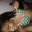 A person in a green and white checkered bikini top lies on their back with dark hair spread out, eyes open looking upward.