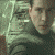 A person in a dark green turtleneck sweater appears against a light gray background with faint lines, showing subtle facial expression changes across frames