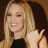 Static 48x48 pixel icon showing a smiling woman with long blonde hair wearing a black top, cropped to show upper body and hand gesture against dark background.