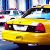 Yellow taxi cab with red accents and visible headlights, set against a blurred urban background.