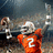 A football player in an orange jersey with number 2 raises both arms in a celebratory pose against a blurred stadium background.