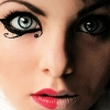 Close-up of a person's face with stylized black eye makeup featuring winged eyeliner and a small decorative swirl near the lower eyelid, red lips, and visible nose.
