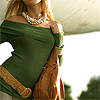 A person wearing a green off-shoulder top, a wide brown belt, and a white pearl necklace, holding a brown bag.