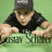 Pixelated image of a person in black shirt and dark cap leaning forward with arms extended, green background, partial text visible below.