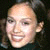 Pixelated close-up of a smiling person with light skin tone, dark hair visible on the right side, and no discernible clothing or background details.