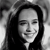 Black-and-white pixelated image of a person with long dark hair, closed eyes, and a slight smile, cropped to show shoulders and upper chest.