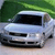 A light blue sedan with dark windows and visible headlights is positioned on a light surface against a green background.