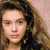 Pixelated close-up of a person with light skin tone, brown hair, and neutral expression against a soft pink background.