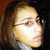 Pixelated close-up of a person with light skin wearing glasses, brown hair, and a white top against dark background.