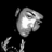 Pixelated grayscale icon of a stylized character with large eyes and a bright white mouth area against black background.