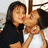 Two people in close physical contact, one in dark clothing kissing the other in light clothing on a light background.