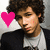A person with curly brown hair wears a dark jacket over a light shirt, positioned against a neutral background with four colored heart icons in different corners.