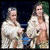 Two women in white robes stand side-by-side on a dark stage with green foliage behind them, while a third woman in a light dress appears separately against black background.