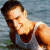 Pixelated image of a person with dark hair wearing a sleeveless top, leaning forward against a blurred blue-gray background.