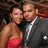 Two people pose closely together; one wears a red strapless dress, the other a dark suit with a white shirt and tie.
