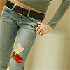 A person wearing light blue denim jeans with a brown belt and a gray long-sleeve top, showing a hand with red nail polish near the waist.