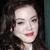 A pixelated close-up of a person with dark curly hair, light skin, and red lips, set against a dark background with a teal vertical element on the right.