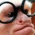 A close-up of a person wearing dark-rimmed glasses with a red dot on the nose, showing two where text appears below