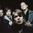 Pixelated group photo of four people on left, white text "Taking Back Sunday" and heart symbol on right against black background.