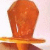 A pixelated orange figure with a rounded head and vertical white stripe on the face, standing against a light pink background.
