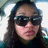 Pixelated close-up of a person with long dark hair wearing dark sunglasses, pink lips, and a dark top against a light background.