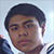 Pixelated close-up of a person with short dark hair, light skin tone, and neutral expression wearing a white-collared shirt against light background.
