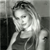 Black-and-white pixelated image of a person with light-colored hair, wearing a dark sleeveless top, positioned against a gradient background.