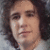 Pixelated close-up of a person with dark curly hair and light skin, wearing a white garment against a blurred background.