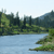 Pixelated landscape with blue water, green vegetation, and dark trees under a light sky.