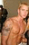 Static pixelated image of a shirtless person with light skin tone, brown hair, and dark clothing on the left side against a muted background.