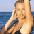 Pixelated static image of a person with light brown hair in swimwear against an ocean background, viewed from the side with one arm raised and hand near face.
