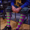 A person in blue shirt and dark pants sits with legs crossed, wearing purple-green diamond-patterned socks; text overlays change position across frames.