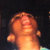 Pixelated close-up of a person's face with closed eyes, warm orange and brown tones, dark background, and visible pixelation artifacts.