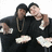 Two figures in black hooded garments with white accents pose closely together against a plain background.