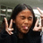 A pixelated image shows a person with dark hair making a peace sign with their right hand, wearing a dark top against a blurred background.